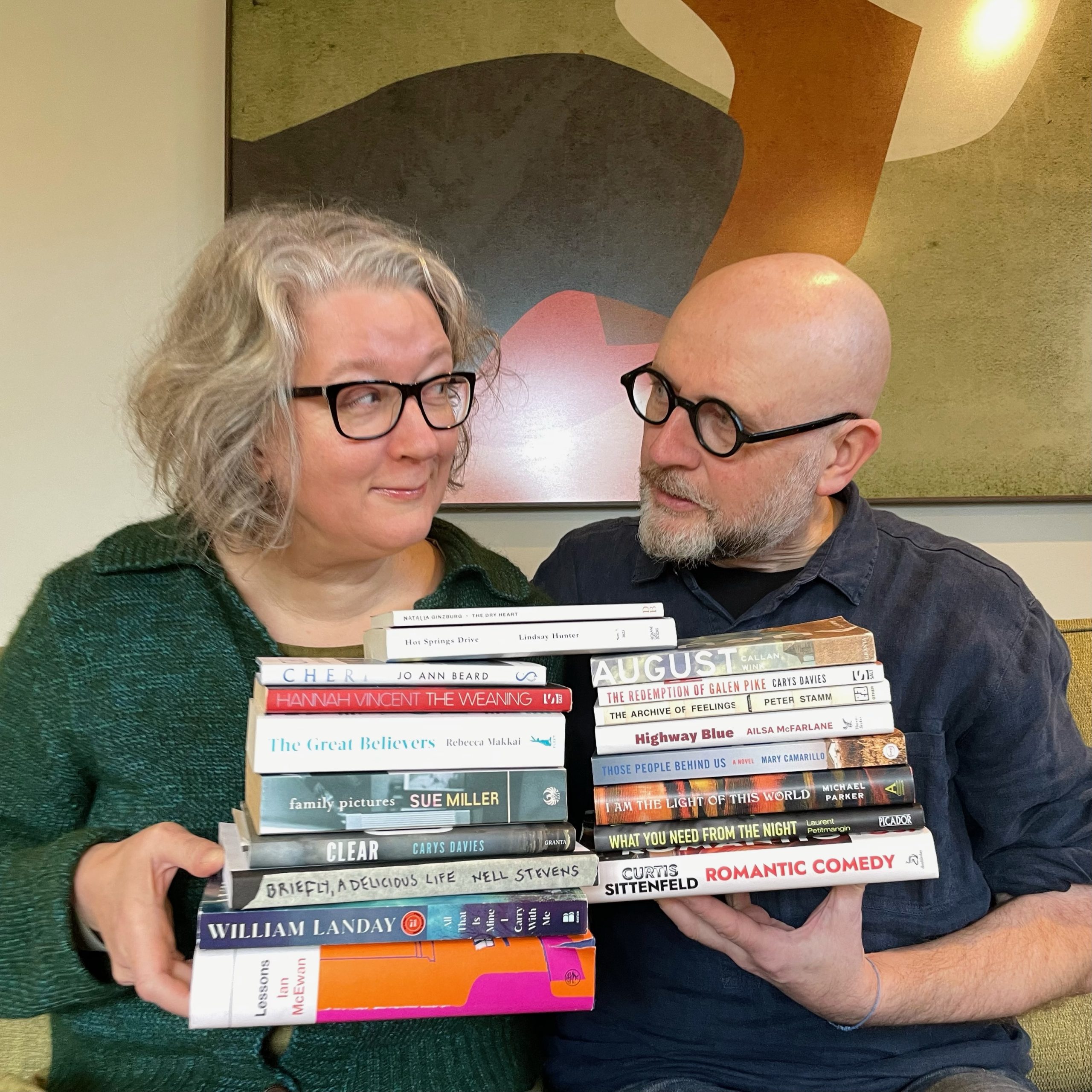 Man and Woman wearing glasses and holding stacks of books